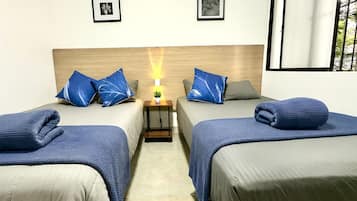 Una habitación de hotel con dos camas, una mesita de noche con una lámpara y cuadros en la pared.