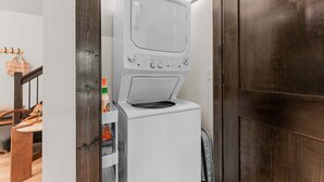 Une petite machine à laver à chargement frontal, de couleur blanche, installée dans une petite buanderie avec une porte en bois et un mur blanc.