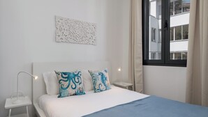 A bedroom with a bed, two pillows, a bedside table, a lamp, a window, and a wall decoration. - Funchal Oh My! - Cozy Stay with Terrace (Funchal)