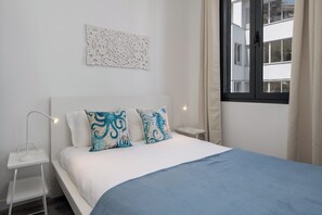 Ein Schlafzimmer mit einem Bett, zwei Kissen, einem Nachttisch, einer Lampe, einem Fenster und einer Wanddekoration.