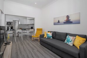 Ein modernes Wohnzimmer mit einem grauen Sofa, gelb-blauen Kissen, einem gelben Sessel und einem Gemälde mit gestapelten Steinen an der Wand.