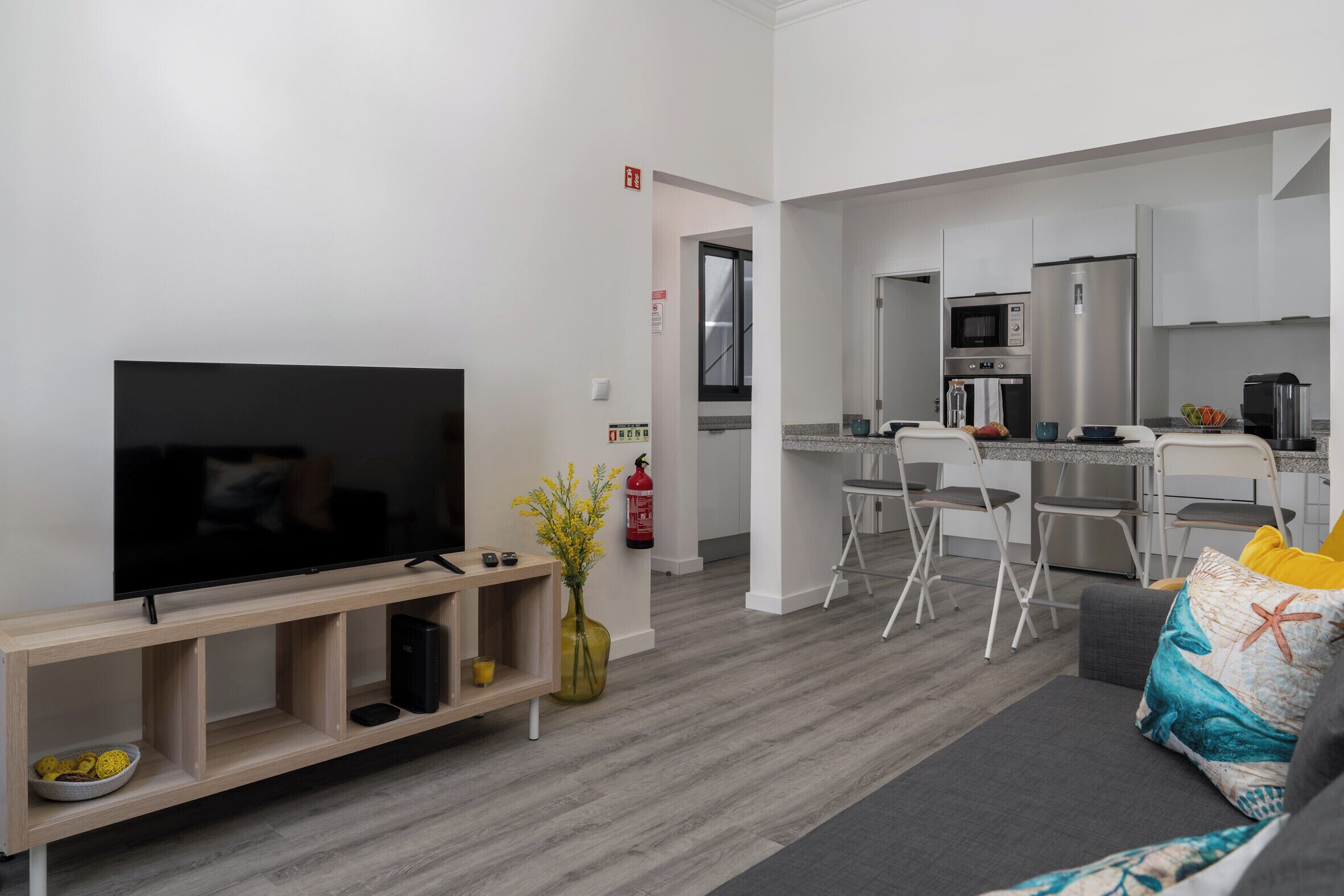 A modern living room with a flat-screen TV, a wooden entertainment unit, and a sofa with decorative pillows.