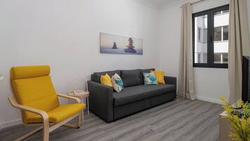 A living room with a grey sofa, yellow armchair, and a painting of stacked stones.