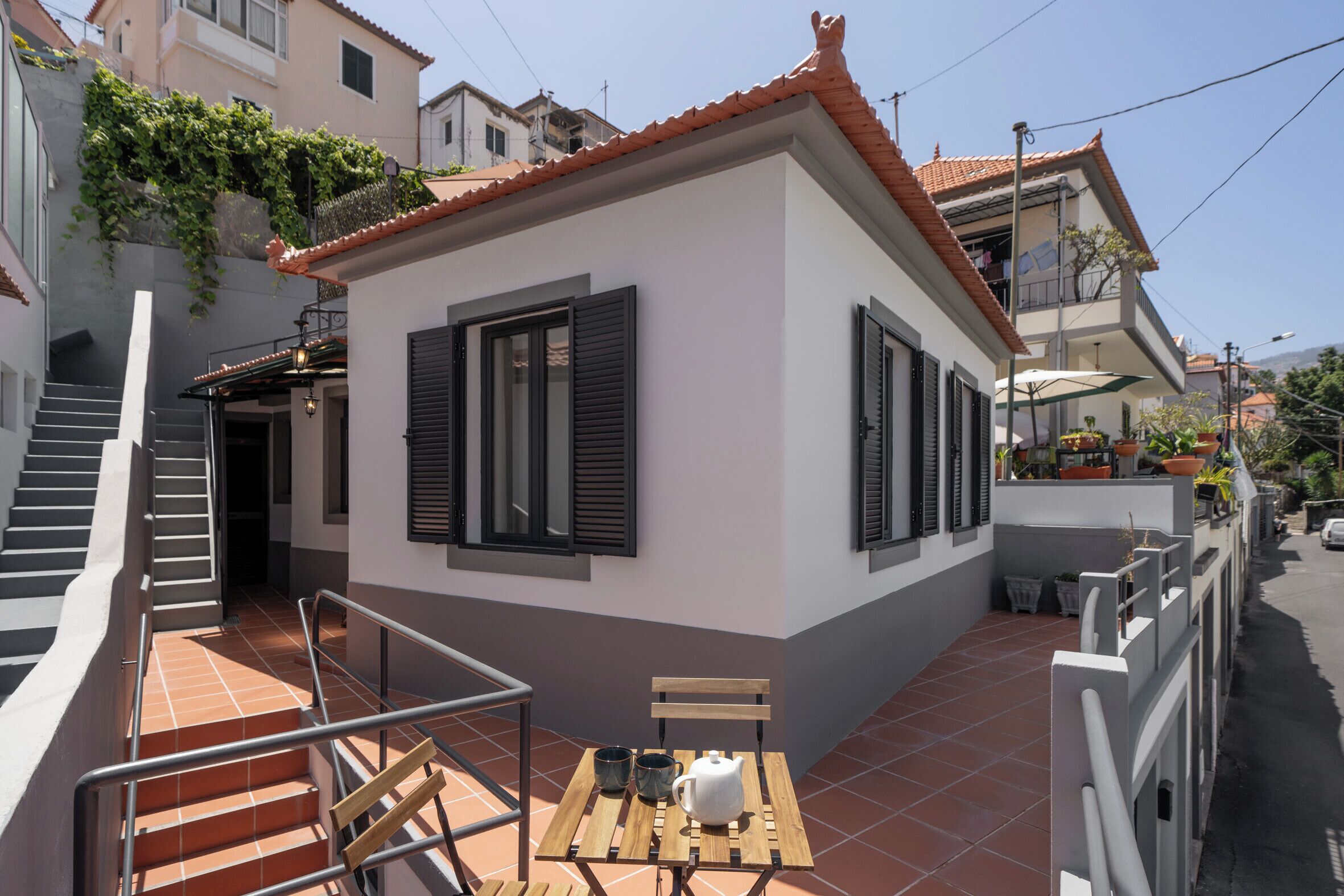 A small, single-story building with a tiled roof, a staircase leading to an upper level, and a small outdoor seating area with a table and chairs.