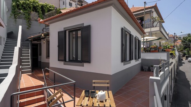 A small, single-story building with a tiled roof, a staircase leading to an upper level, and a small outdoor seating area with a table and chairs. - Funchal Oh My! - Cozy Stay with Terrace (Funchal)