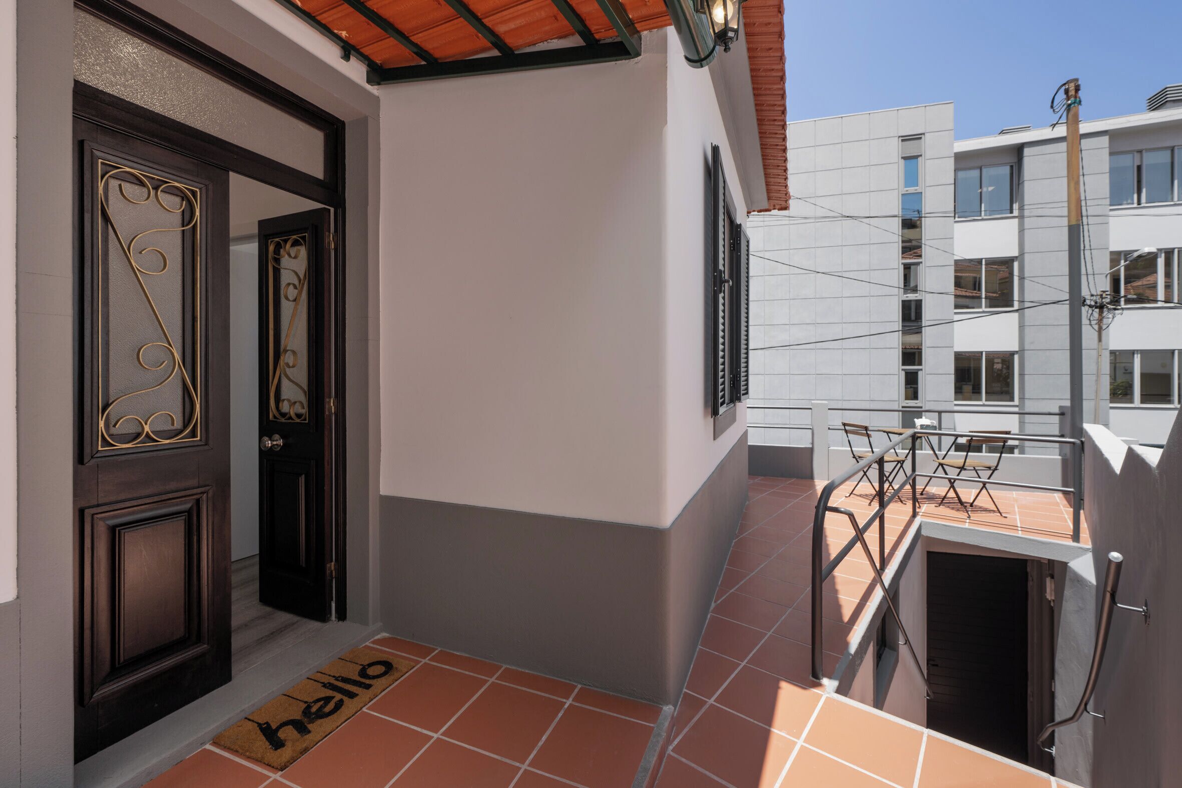 A residential building with a balcony, a door with decorative glass panels, and a 'hello' mat at the entrance.