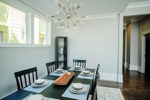 A dining area with a table set for six, a modern chandelier, and a view of the outside through large windows.