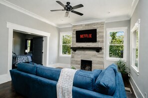 A living room with a blue sofa, a fireplace, a mounted TV, and a ceiling fan.