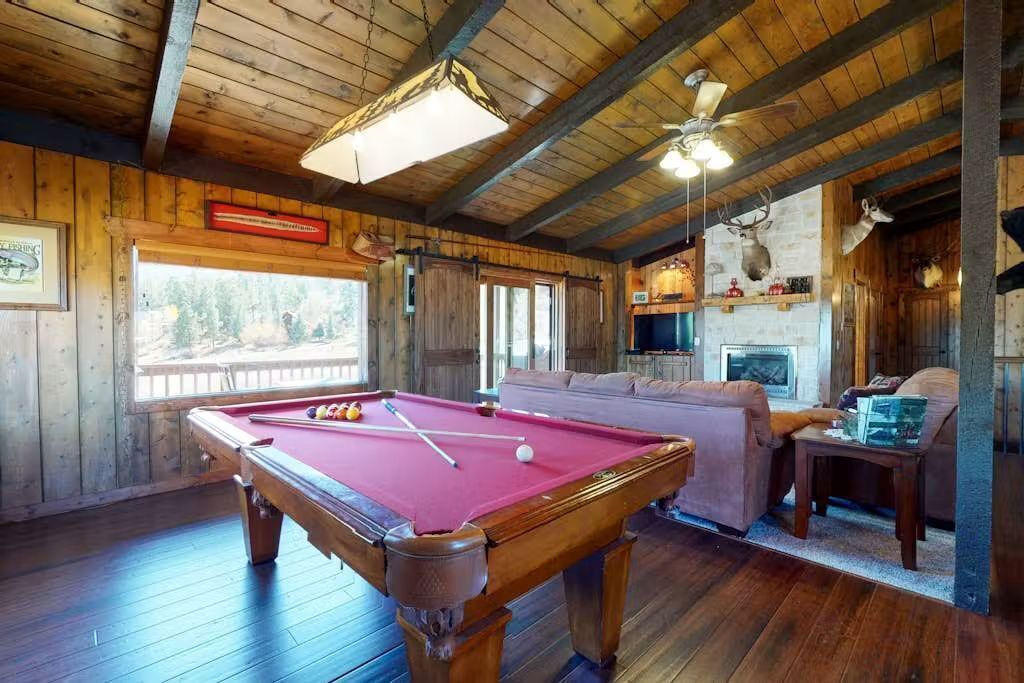 Un interior de madera con una mesa de billar, un sofá y una chimenea.