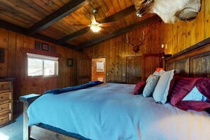 Een houten kamer met een bed, een plafondventilator en een opgehangen hertenkop.