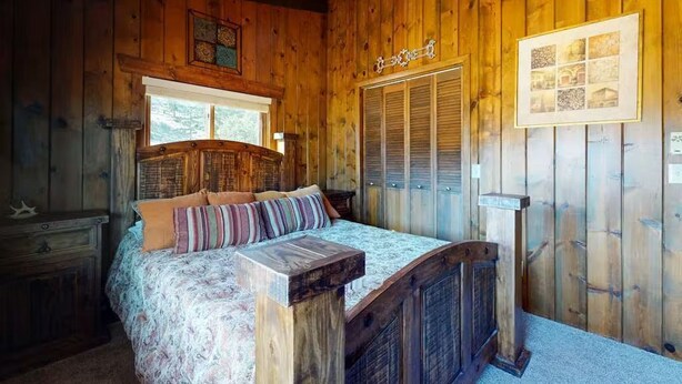 A wooden cabin bedroom with a bed, a nightstand, a dresser, and a window with shutters. - 4 Eagles | Hot Tub | South Fork Cabin | Wolf Creek (South Fork)