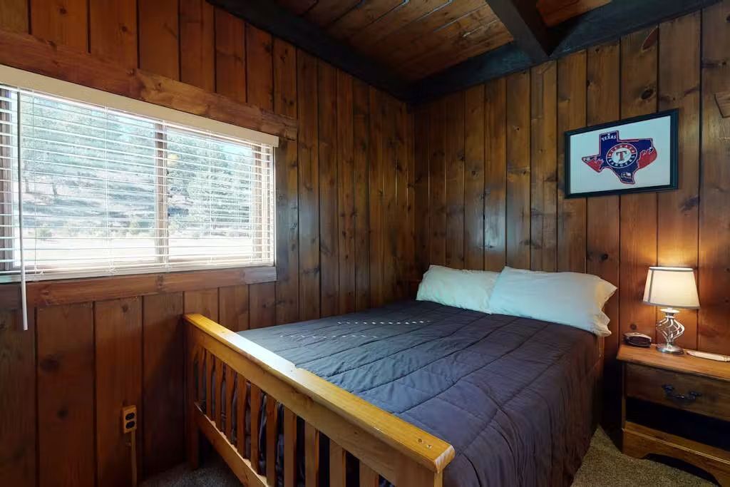 Une pièce aux murs lambrés, comprenant un lit, une table de chevet, une lampe et un drapeau du Texas encadré.