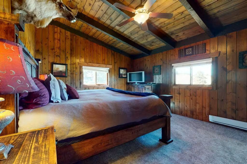 A wooden cabin room with a bed, a ceiling fan, and a television.