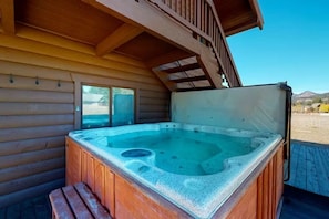Ein Whirlpool vor einer Holzhütte mit einer Holzterrasse und blauem Himmel im Hintergrund.