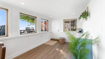 Ein Zimmer mit großen Fenstern, Holzboden, einer Tür und einem Blumentopf.