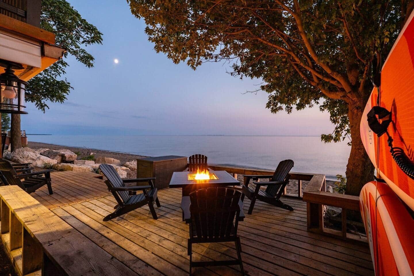 Um deck de madeira com lareira, espaço para sentar e vista para o mar.