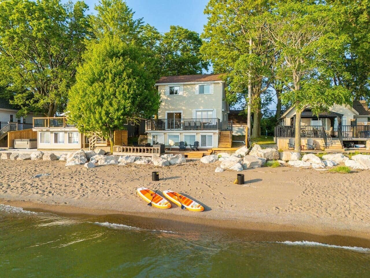 A beachfront property with a two-story house, a wooden deck, and a lifeguard stand on the sand.