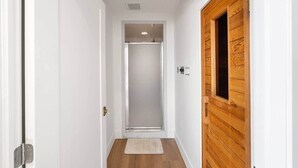 Un corridoio stretto con una porta in legno sulla destra, una porta bianca a sinistra e una porta in vetro alla fine che conduce a una stanza.
