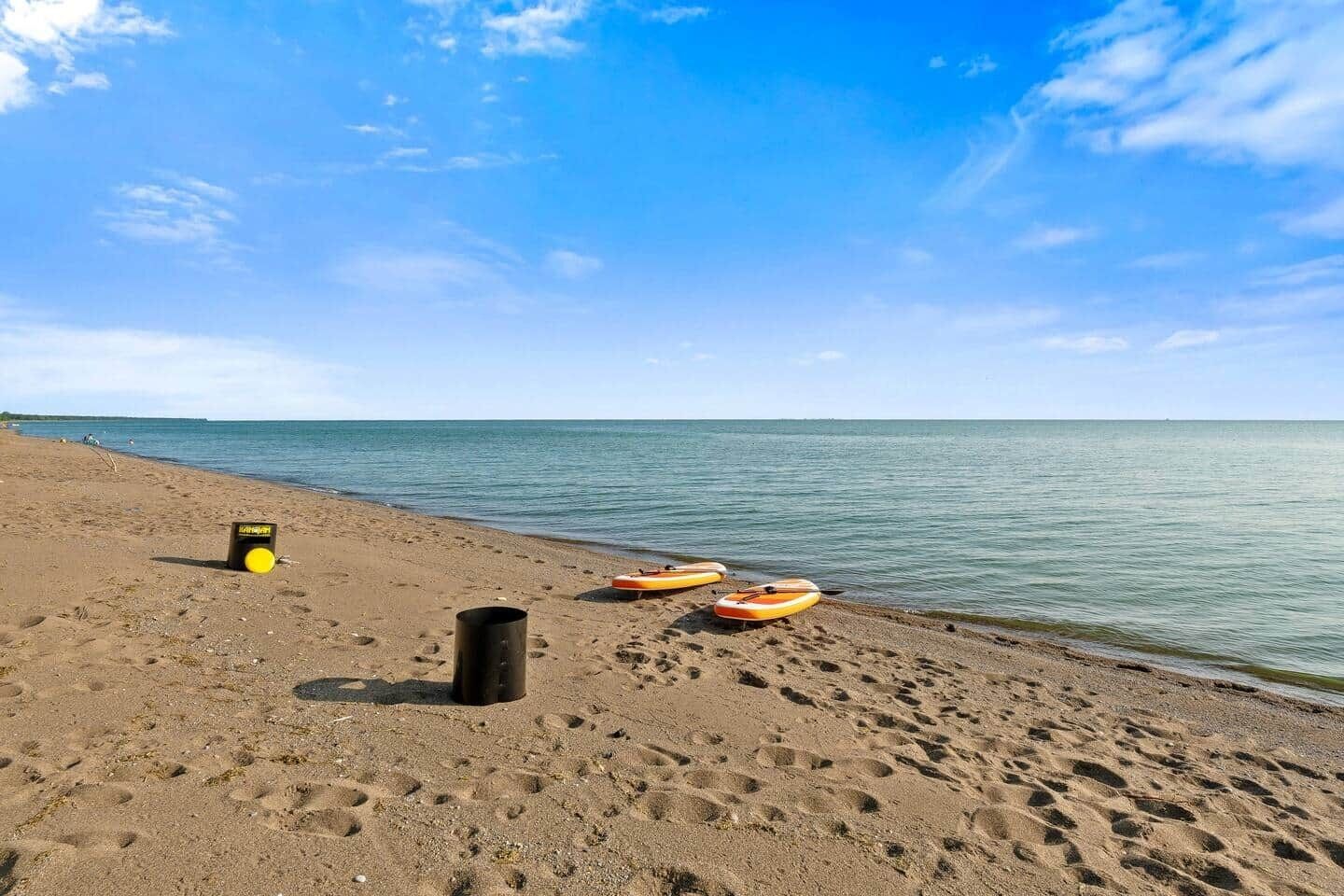 Una playa arenosa con huellas que conducen al agua, un objeto cilíndrico negro y dos kayaks naranja.