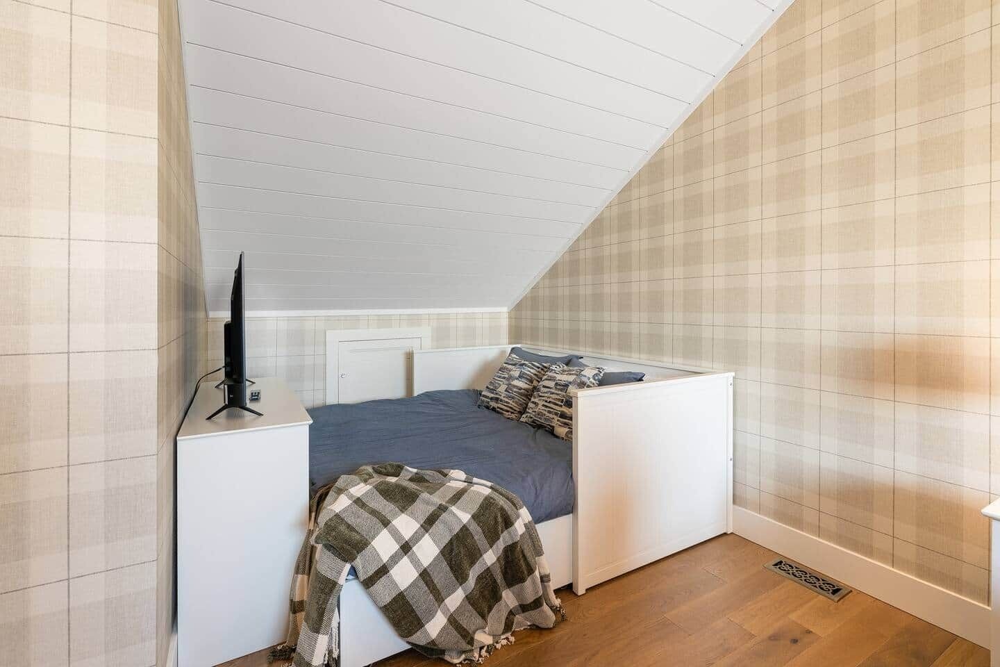 Ein kleines Zimmer mit einem Einzelbett, geneigter Decke, Nachttisch und Fernseher.