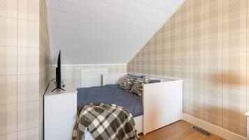 Ein kleines Zimmer mit einem Einzelbett, geneigter Decke, Nachttisch und Fernseher.