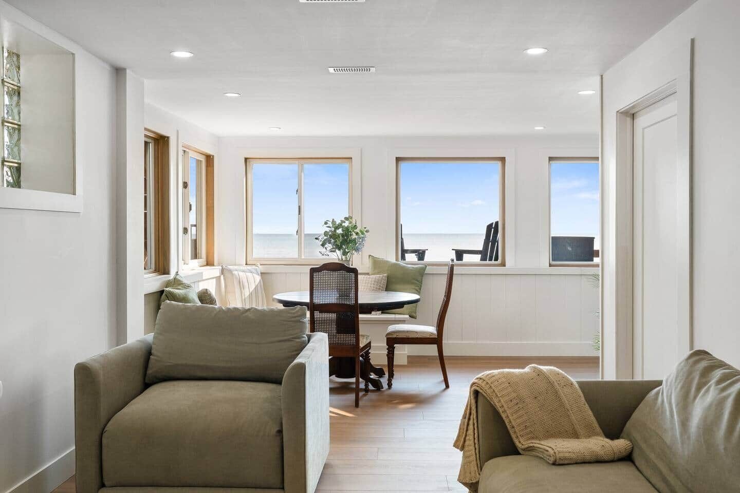 Un salon moderne avec un coin repas, de grandes fenêtres et une vue sur la mer.
