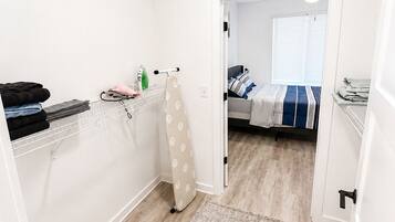 A compact bedroom with a bed, a small ironing station, and a door leading to another room.