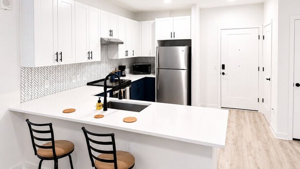 Una cocina moderna con muebles blancos, un refrigerador de acero inoxidable y una isla central con taburetes de bar.