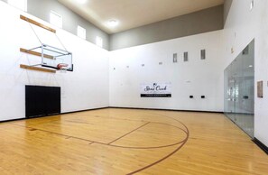 A basketball court with a wooden floor, a basketball hoop, and a sign for Stone Creek Premier Apartments. - Resort-Style 1BR Pool, Gym & Movie Theater (Conroe)