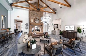 A spacious lounge area with a stone wall, a chandelier, and a seating arrangement including sofas and chairs. - Resort-Style 1BR Pool, Gym & Movie Theater (Conroe)