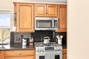 A kitchen with wooden cabinets, a stainless steel microwave, a gas stove, and a kettle. - Mission Beach Oceanfront Penthouse | Wraparound Deck, Fireplace, Garage Parking | Amazing Views (San Diego)