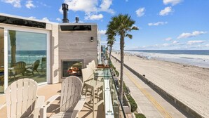 Una propietat a primera línia de platja amb balustrada de vidre, seients exteriors i vista a l'oceà.