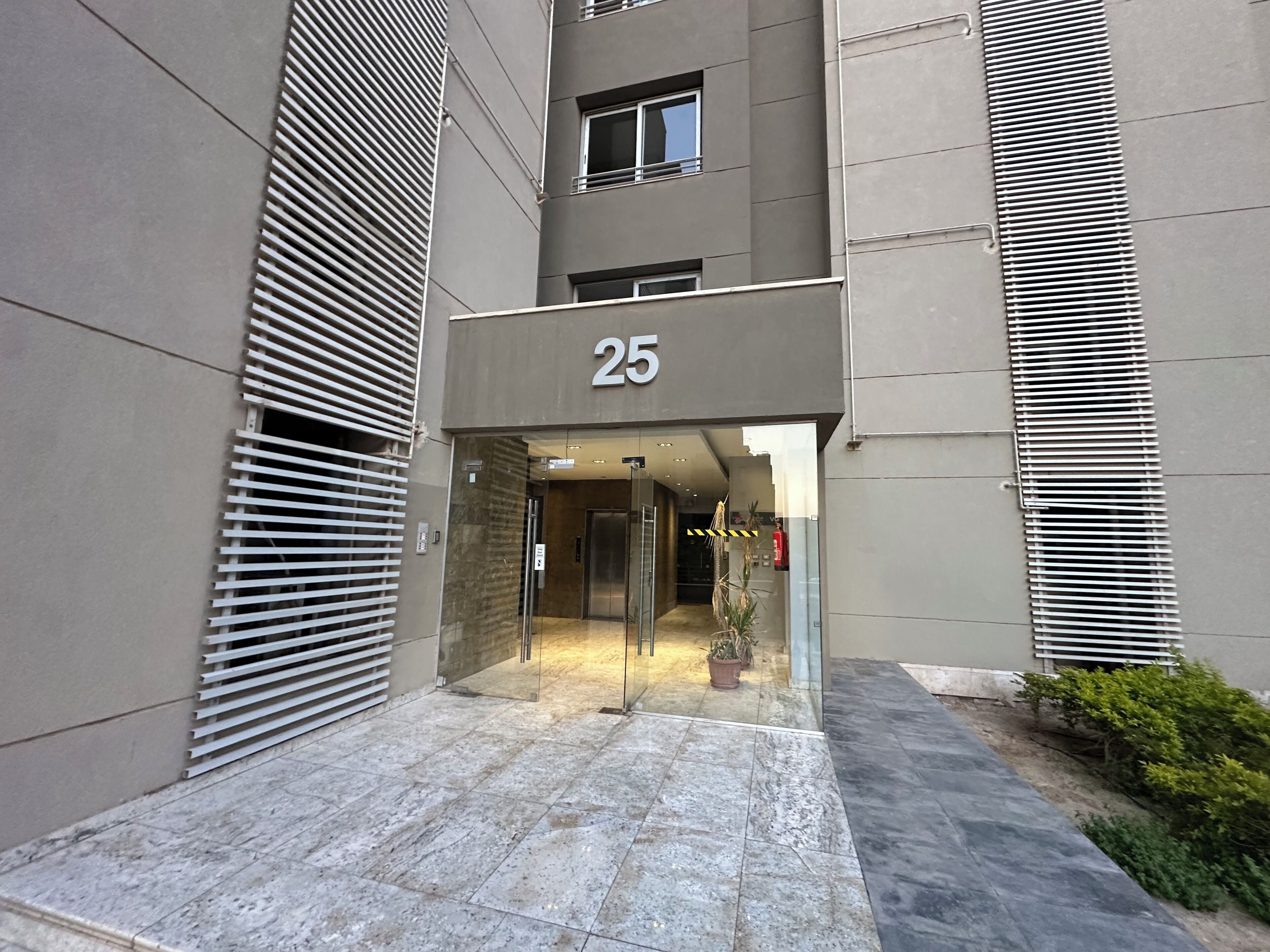 A modern building entrance with a number '25' sign, a glass door, and a potted plant.