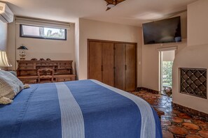 Ein Schlafzimmer mit einem großen Bett, einer Holzkommode, einem an der Wand befestigten Fernseher und einem Boden mit Steinmuster.