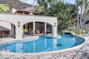 Ein Poolbereich mit steinverkleideter Kante, eine Lounge mit Außensitzgelegenheiten und Blick auf eine gebirgige Landschaft.