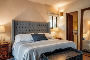Une chambre d’hôtel avec un grand lit, deux tables de chevet avec des lampes, un banc en bois, un miroir et une porte.