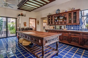 Una cocina con una amplia mesa de madera, piso de baldosas azules y vista al exterior.