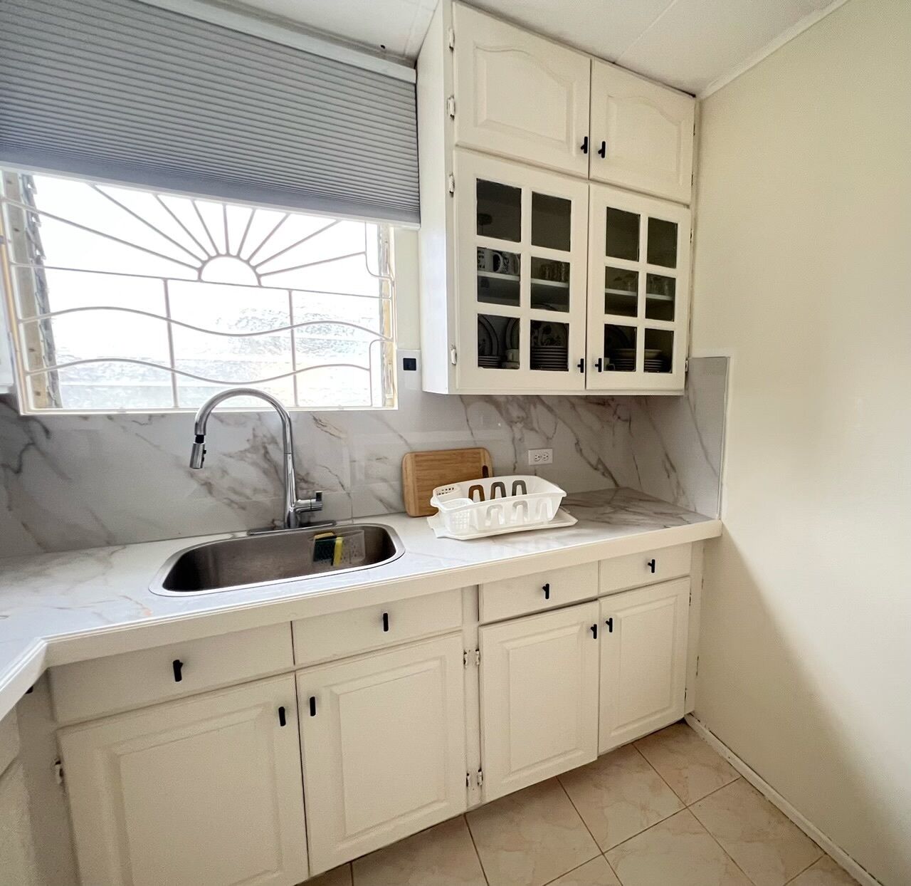 A kitchen with a sink, cabinets, and a window with blinds.