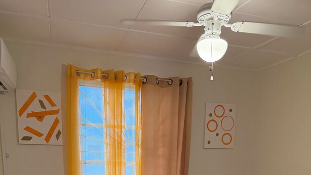 Ein Zimmer mit zwei Betten, einem Deckenventilator und einem Vorhangfenster.