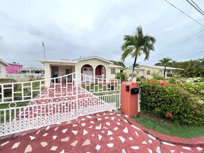 A gated entrance with a mailbox, a pathway leading to a building with a number 176 sign, and a palm tree in the background.