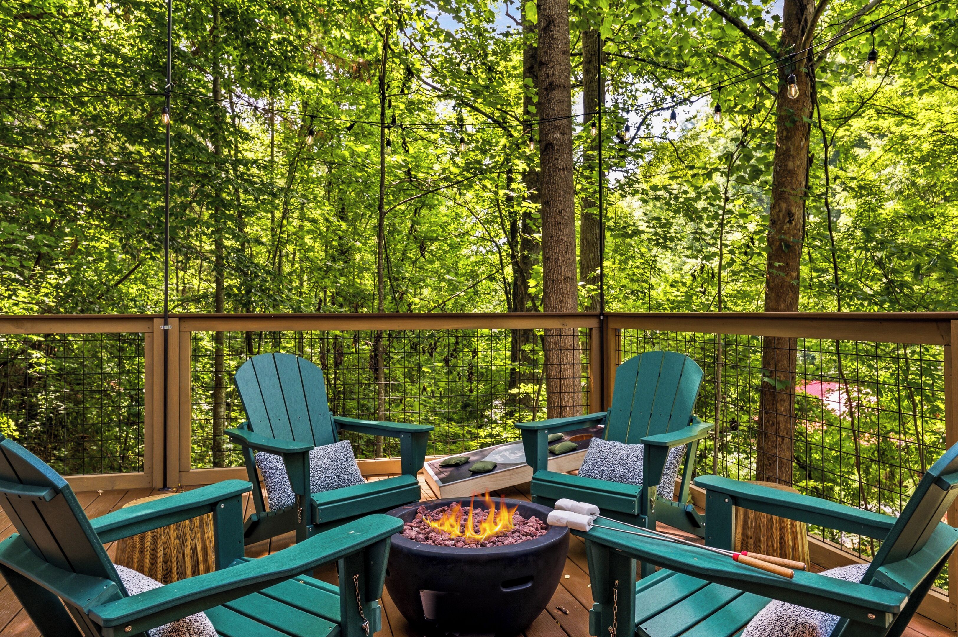 Una terraza al aire libre con sillas Adirondack verdes, un hogar para fogata y vistas a un bosque denso.