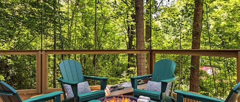 Eine Terrasse im Freien mit grünen Adirondack-Stühlen, einer Feuerstelle und Blick auf einen dichten Wald.