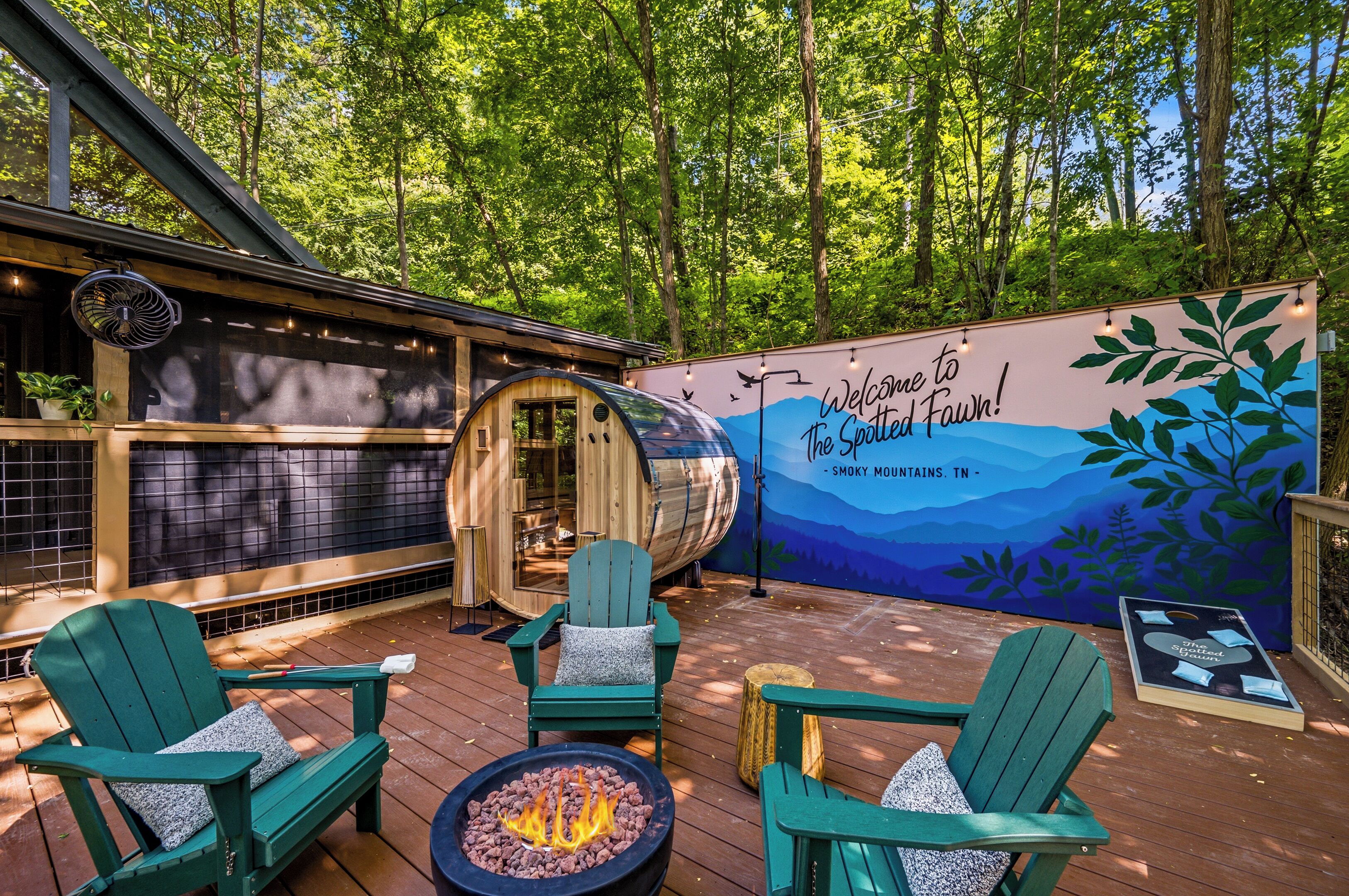 A wooden deck with green Adirondack chairs, a fire pit, and a sauna.