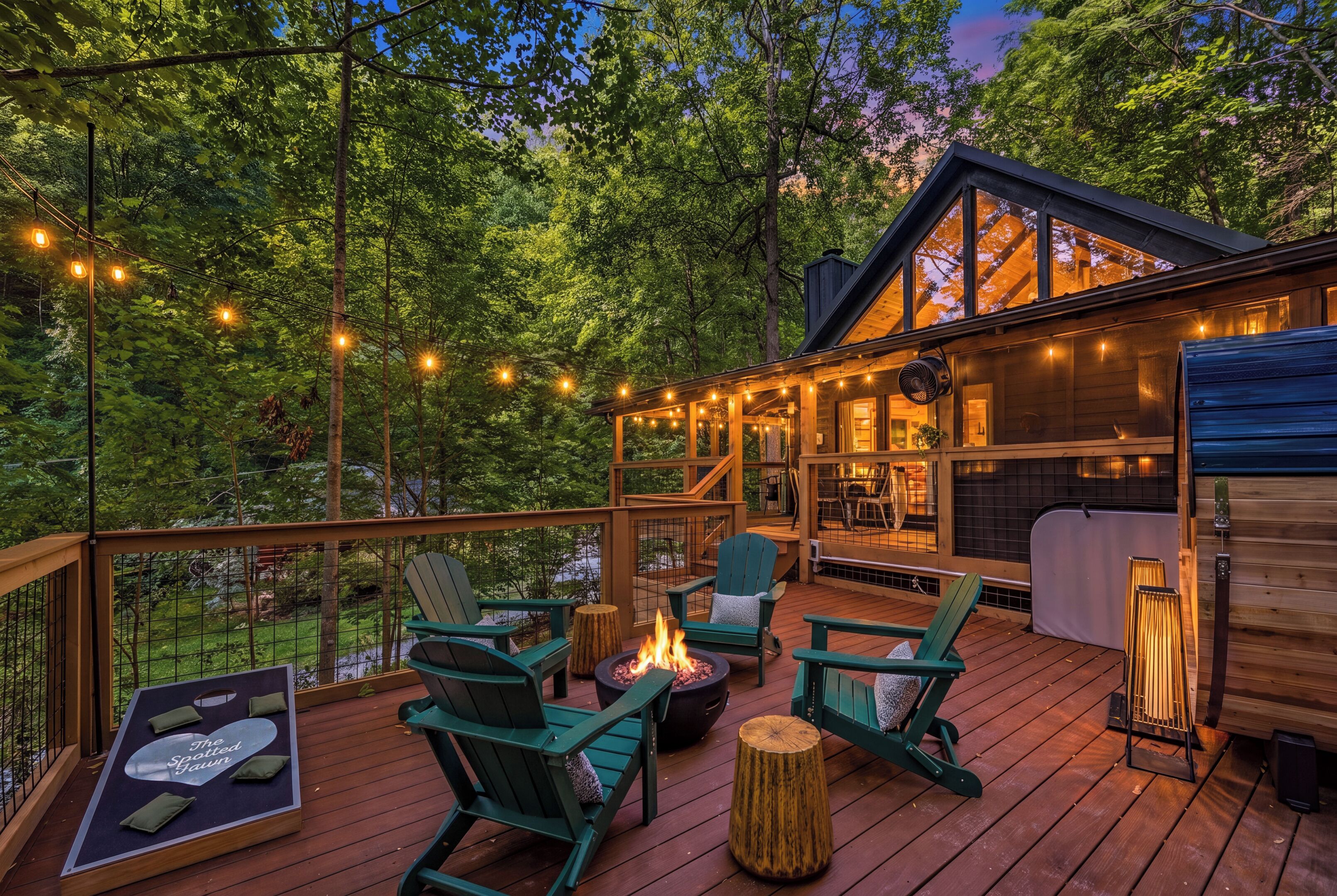 A wooden deck with outdoor seating, a fire pit, and string lights.