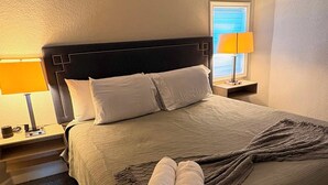 A neatly made bed with a dark headboard, two bedside lamps, and a window with blinds. - Holds 8 · Pool · 3BR/2BA Lower-Unit Duplex Peacock Horse Beach NearbyOut of City (Galveston)