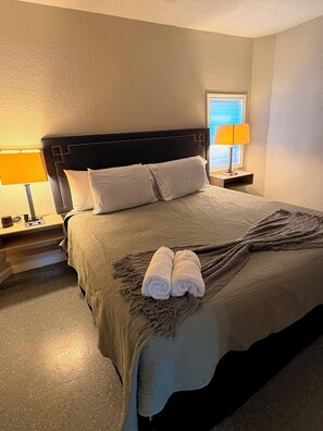 A neatly made bed with a dark headboard, two bedside lamps, and a window with blinds. - Holds 8 · Pool · 3BR/2BA Lower-Unit Duplex Peacock Horse Beach NearbyOut of City (Galveston)