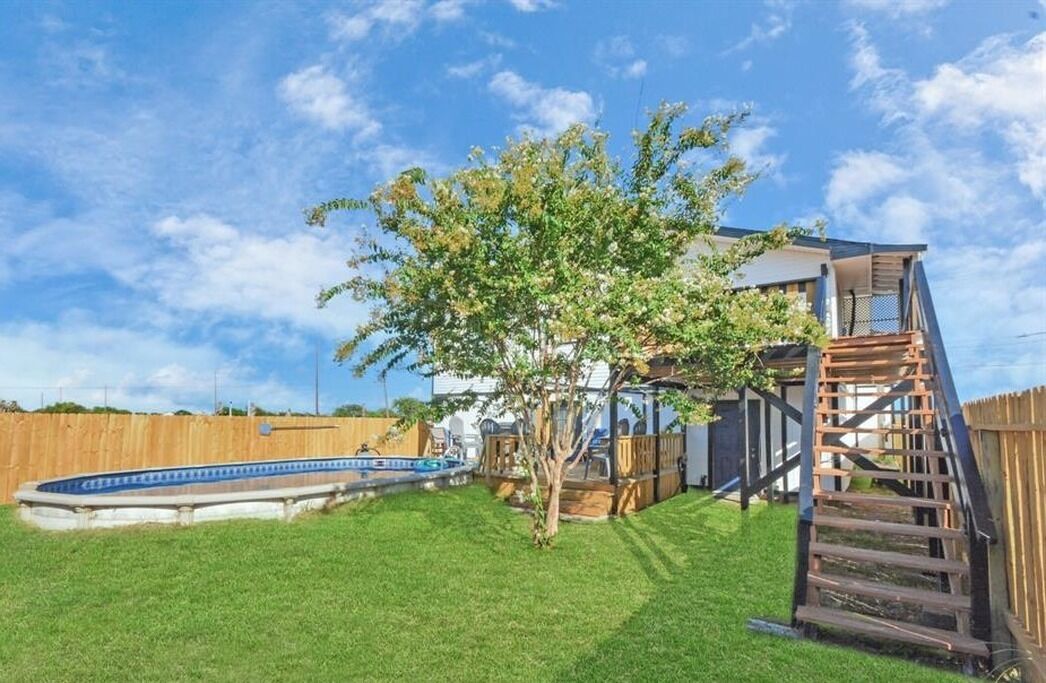 A backyard with a swimming pool, a wooden deck, and a tree.