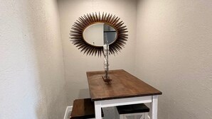 A corner room with a small table and a mirror with a sunburst frame. - Holds 8 · Pool · 3BR/2BA Lower-Unit Duplex Peacock Horse Beach NearbyOut of City (Galveston)