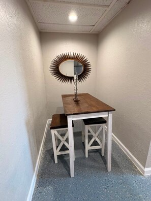 A corner room with a small table and a mirror with a sunburst frame. - Holds 8 · Pool · 3BR/2BA Lower-Unit Duplex Peacock Horse Beach NearbyOut of City (Galveston)