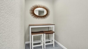 A corner with a white wall, a white table with two wooden stools, and a sunburst mirror above the table. - Holds 8 · Pool · 3BR/2BA Lower-Unit Duplex Peacock Horse Beach NearbyOut of City (Galveston)